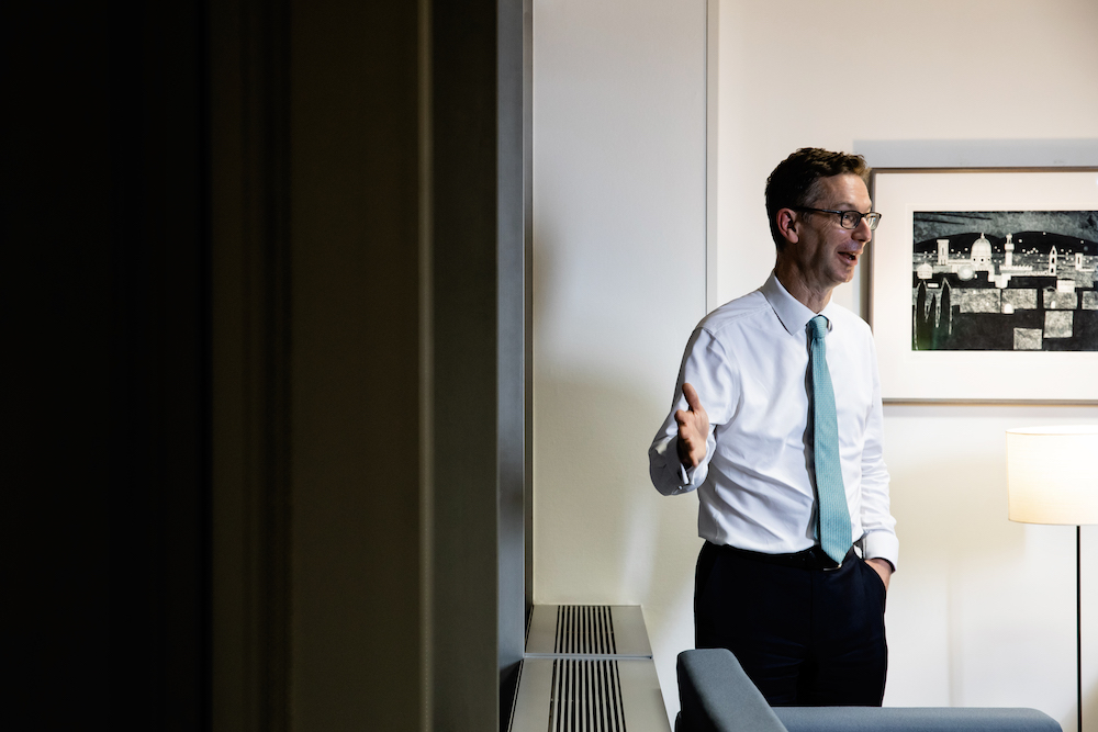 A candid shot of Peter Schofield in an office, laughing, with a painting on the wall behind him